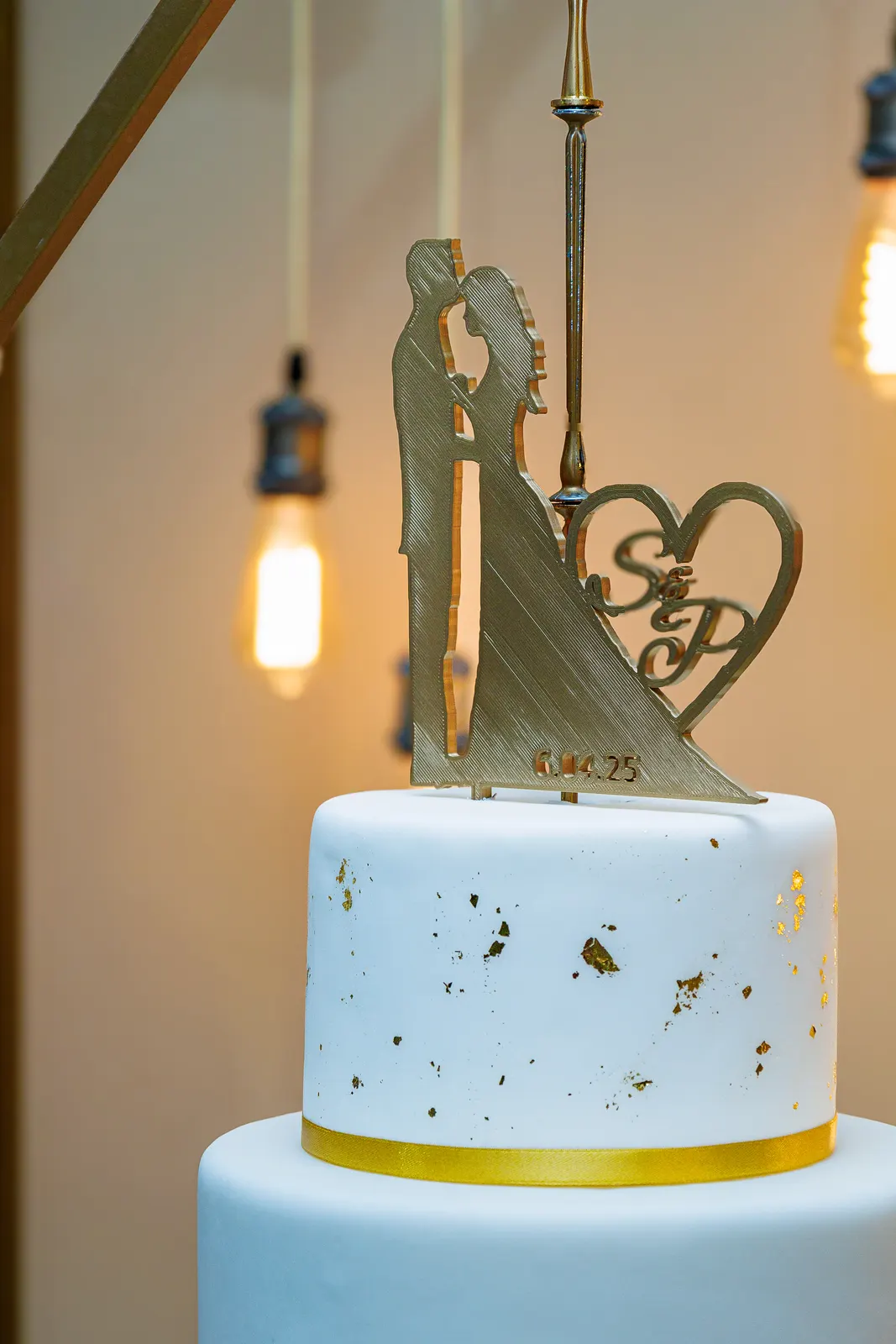 Topo de bolo de casamento branco decorado com detalhes dourados e uma silhueta de noivos