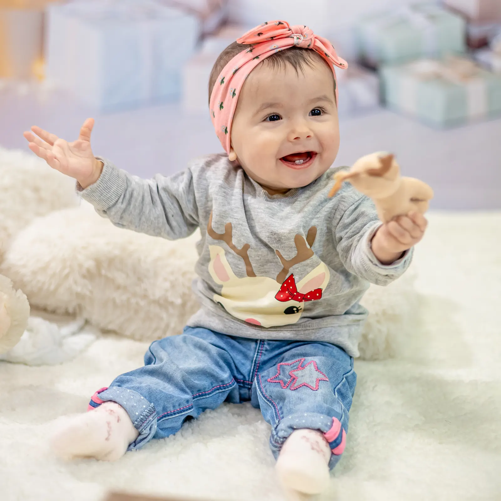 Bebé sorri sentado com uma fita na cabeça e um brinquedo na mão